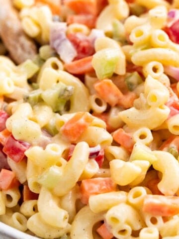 Vegan macaroni salad with crunchy vegetables in a large bowl with a wooden spoon