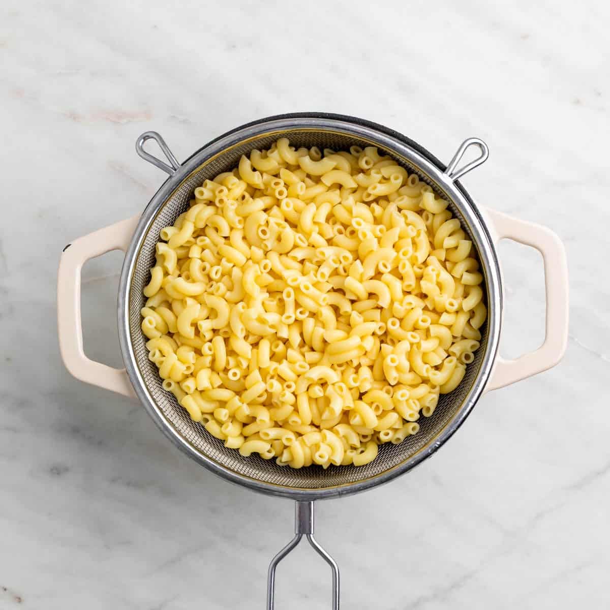 Cooked elbow macaroni draining in a colander over a pot