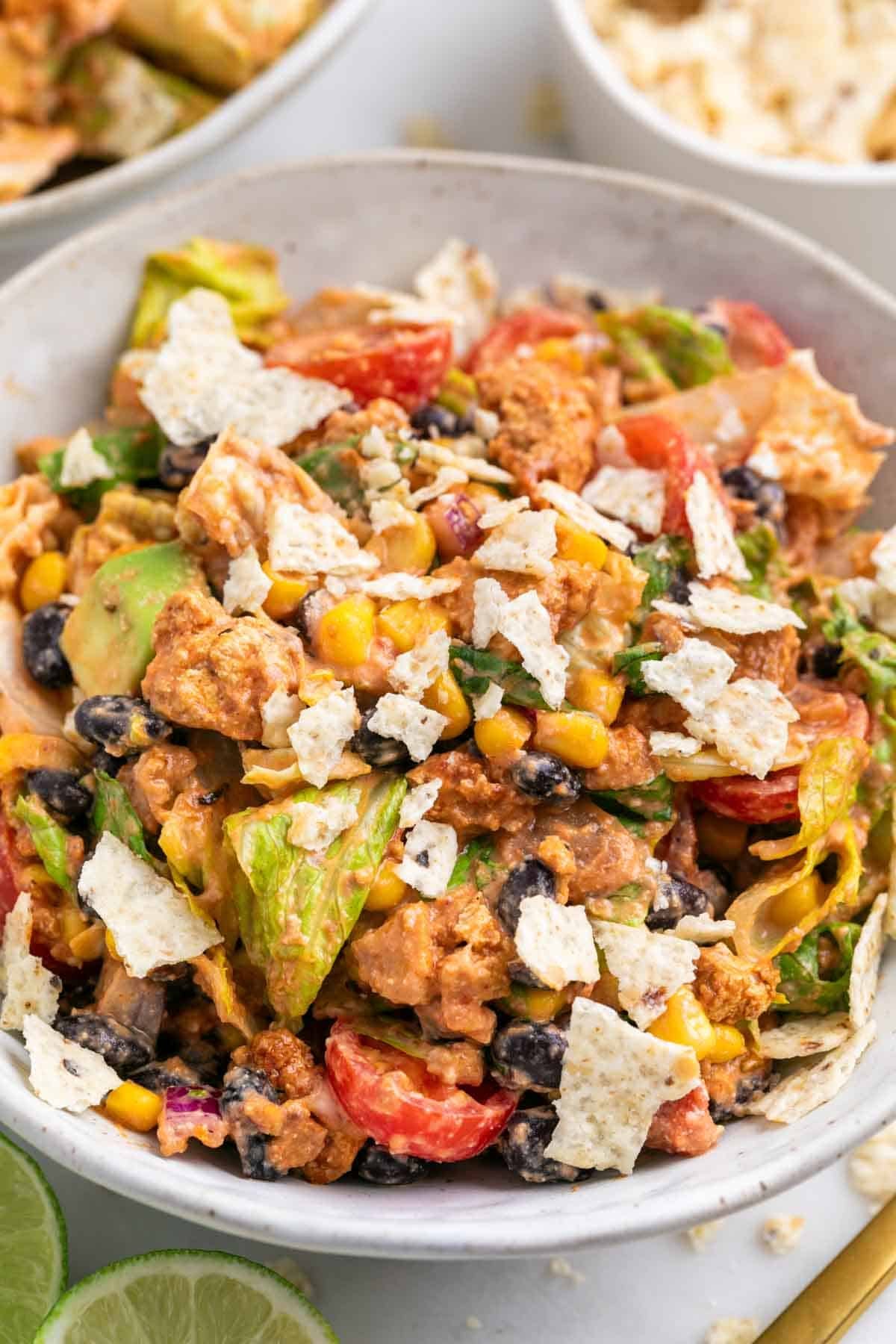Vegan taco salad served in bowls with crushed tortilla chips and lime wedges