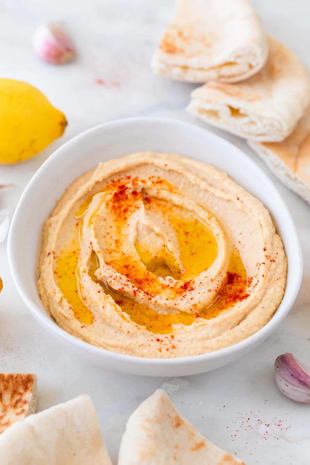 Homemade hummus topped with olive oil and paprika, with pita bread around it