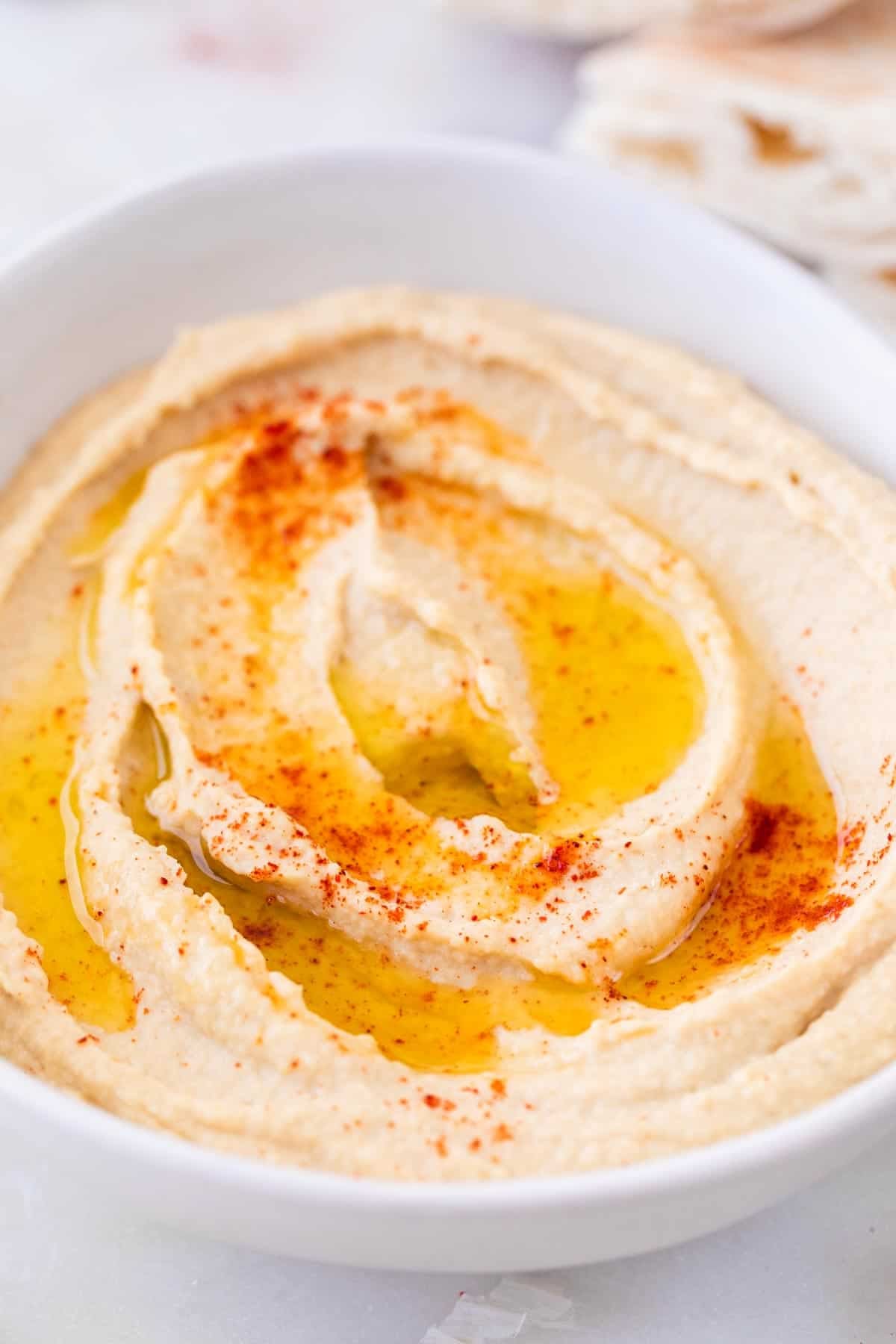 Homemade hummus topped with olive oil and paprika, with pita bread around the bowl