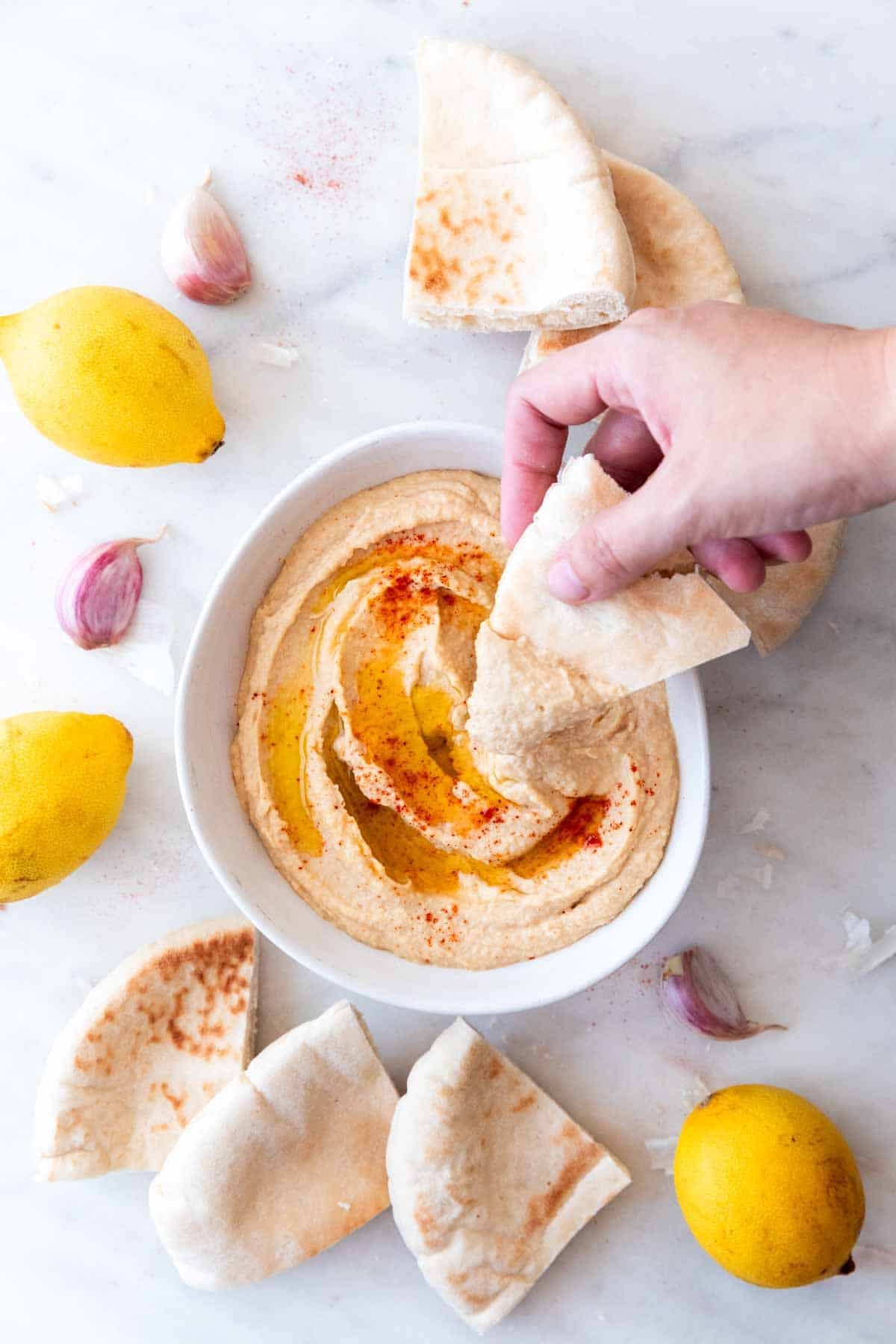 Homemade hummus with a hand dipping pita bread into the bowl