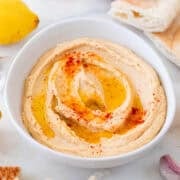 Bowl of homemade hummus with pita bread, lemons, and garlic on the side