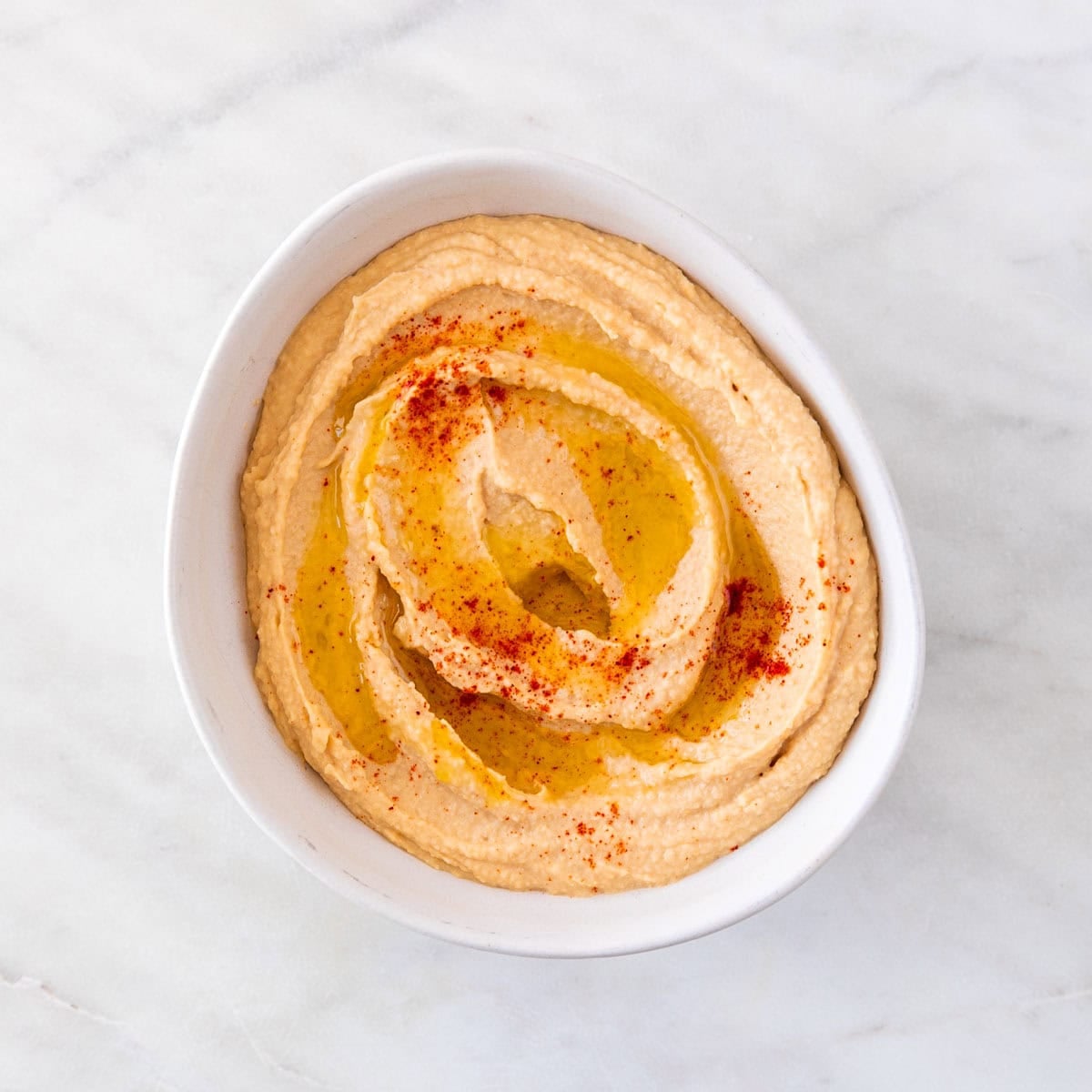 Homemade hummus in a bowl topped with extra virgin olive oil and paprika