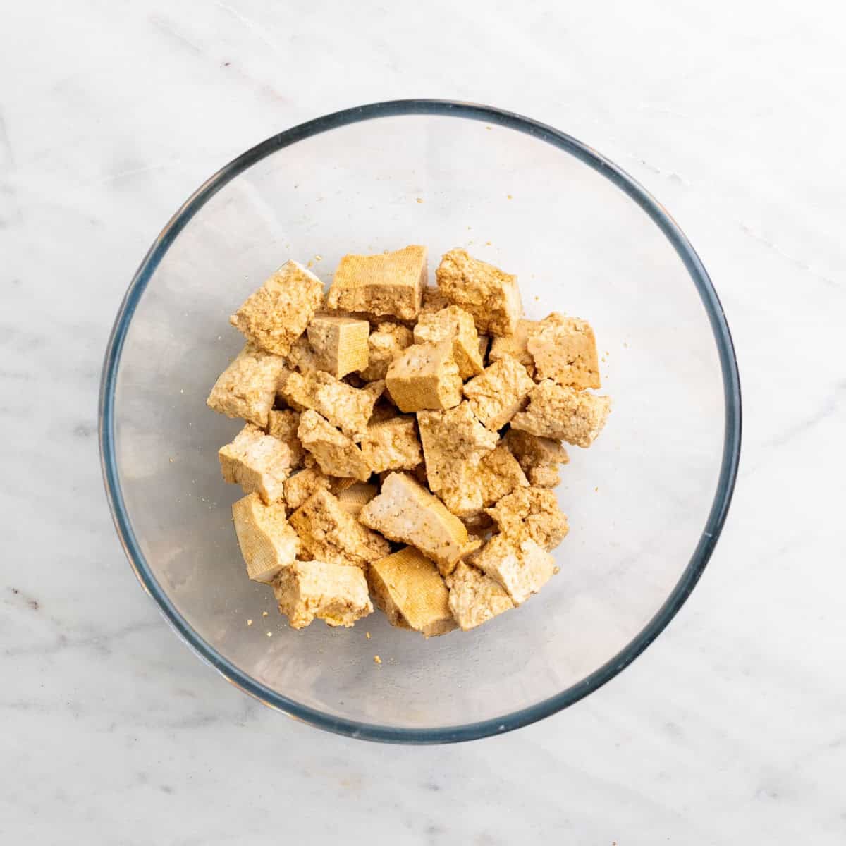 Tofu pieces coated with olive oil and soy sauce in a bowl