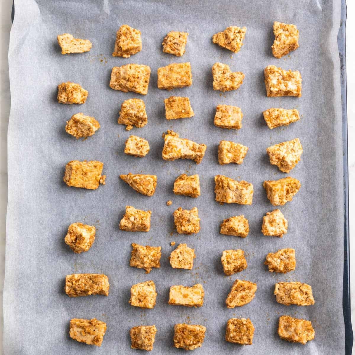 Seasoned tofu pieces arranged on a parchment-lined baking sheet