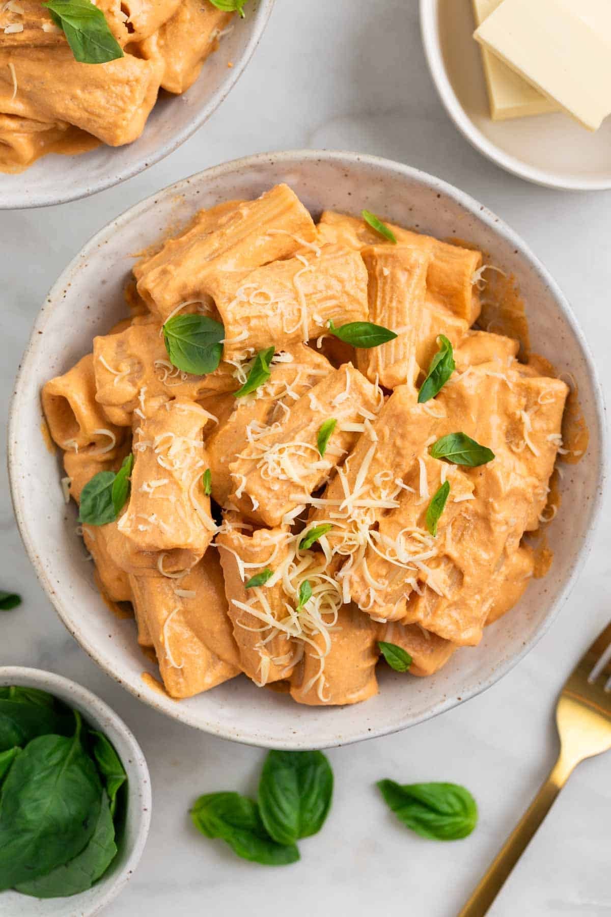 Two bowls of tofu pasta topped with basil and vegan Parmesan