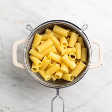 Cooked rigatoni draining in a colander over a pot