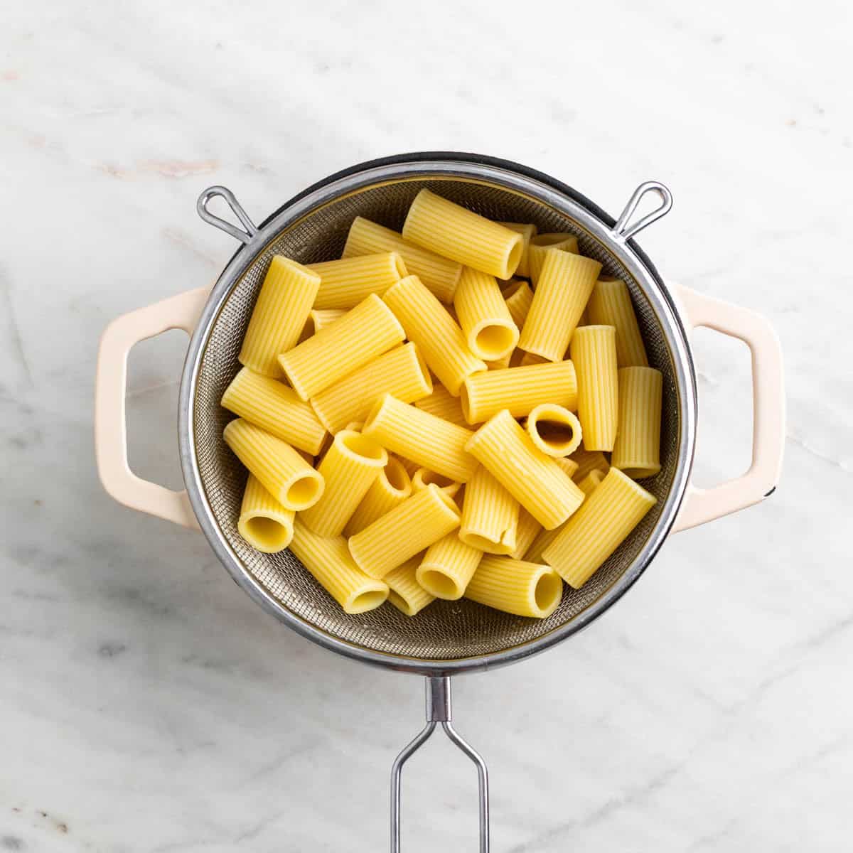 Cooked rigatoni draining in a colander over a pot