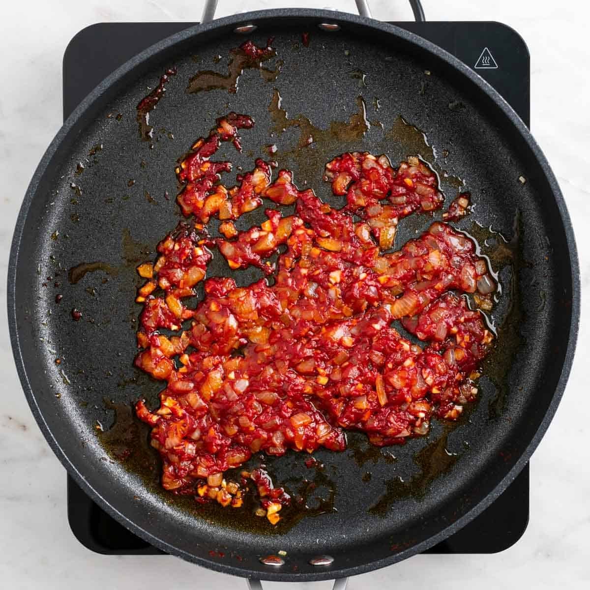 Tomato paste and red pepper flakes cooking with onion and garlic