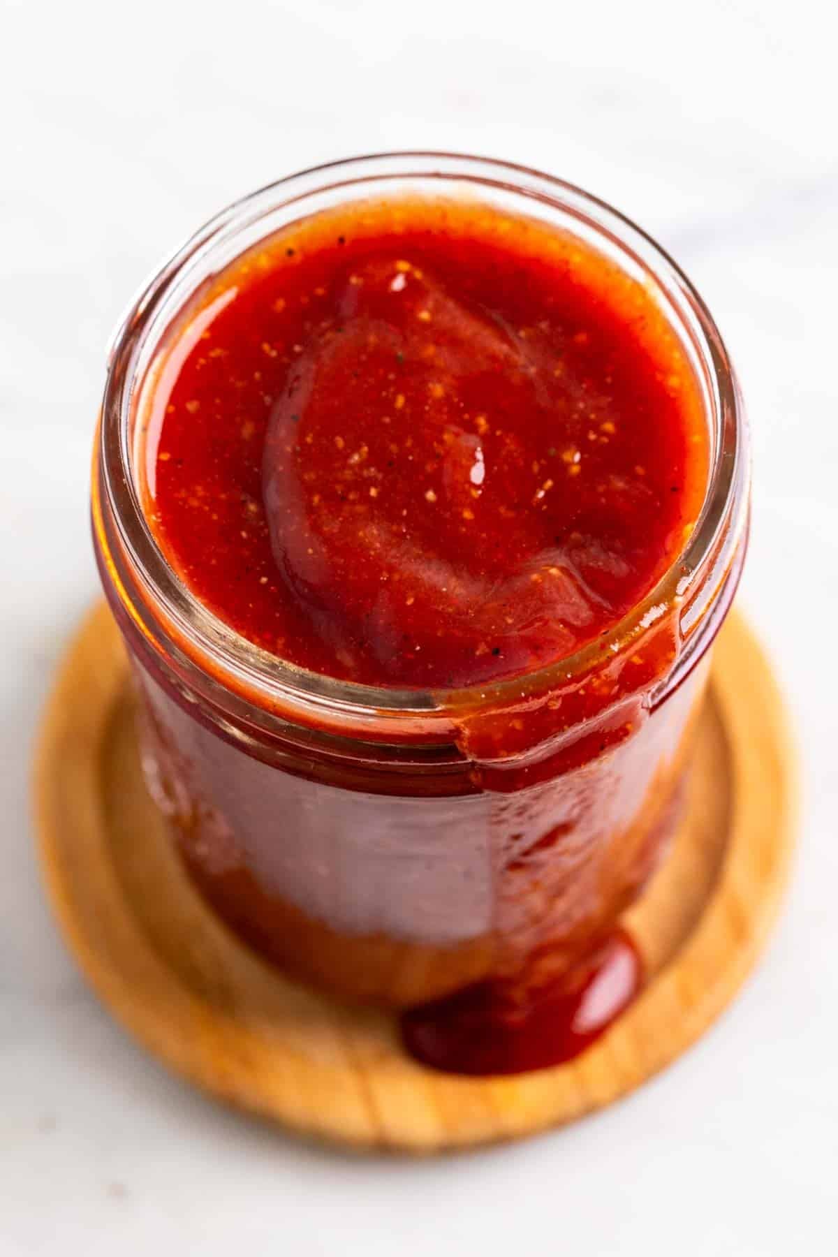 Vegan BBQ sauce dripping from a glass jar onto a wooden coaster