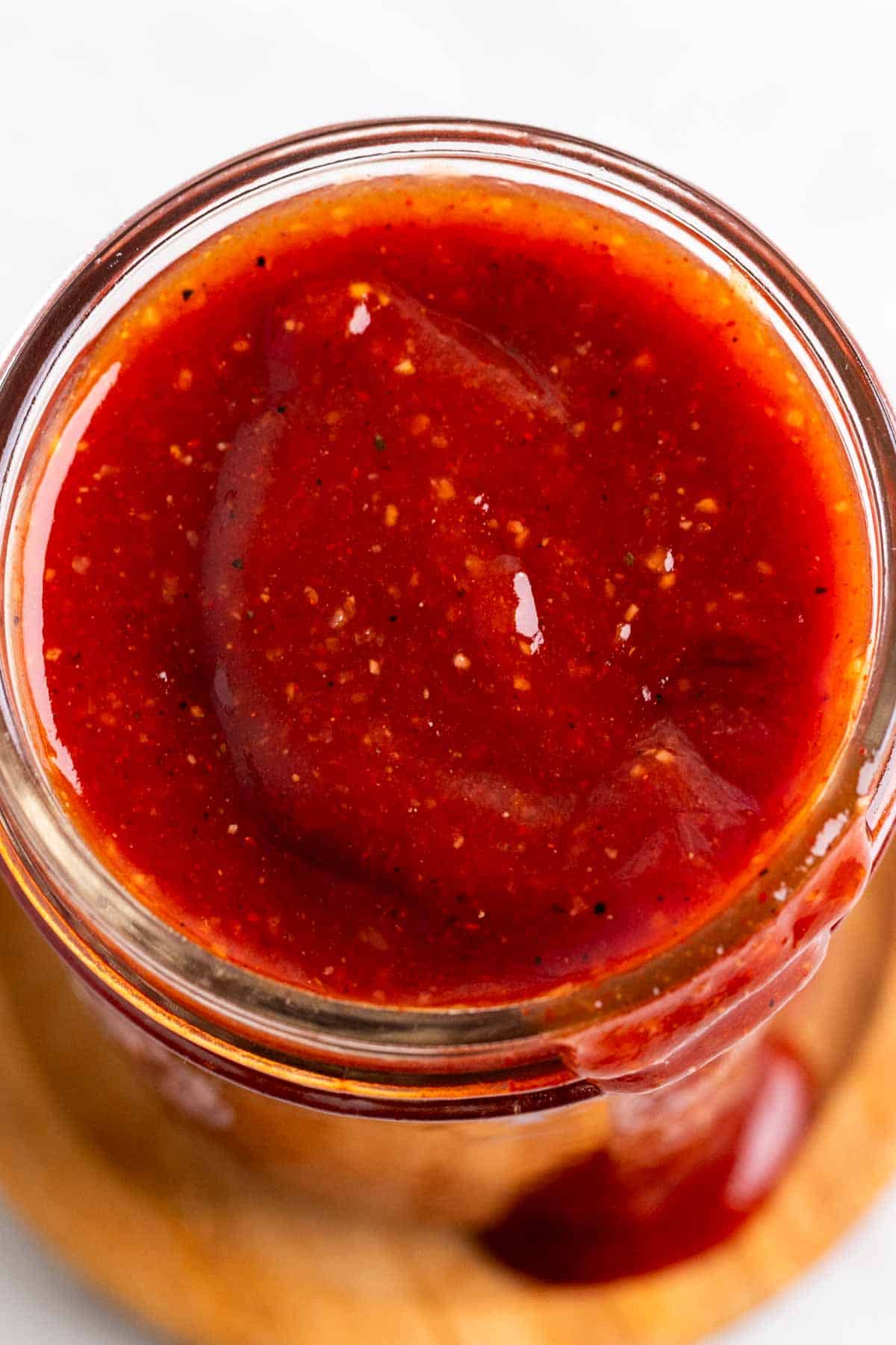 Glass jar filled with vegan BBQ sauce dripping over a wooden coaster