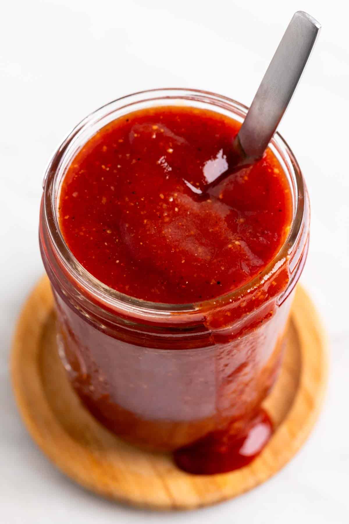 Vegan BBQ sauce in a glass jar with a spoon inside