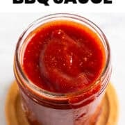 Homemade vegan BBQ sauce spilling down a jar onto a wooden coaster