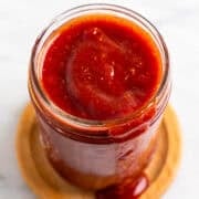 Jar of smoky vegan BBQ sauce dripping onto a wooden coaster