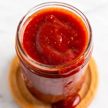 Jar of smoky vegan BBQ sauce dripping onto a wooden coaster