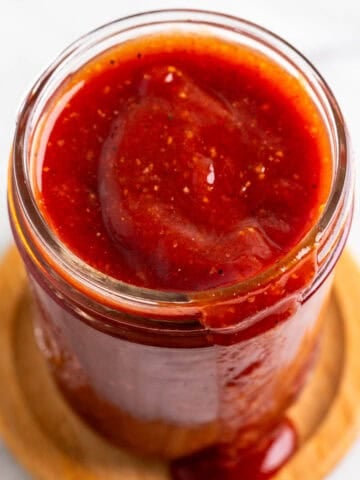 Jar of smoky vegan BBQ sauce dripping onto a wooden coaster