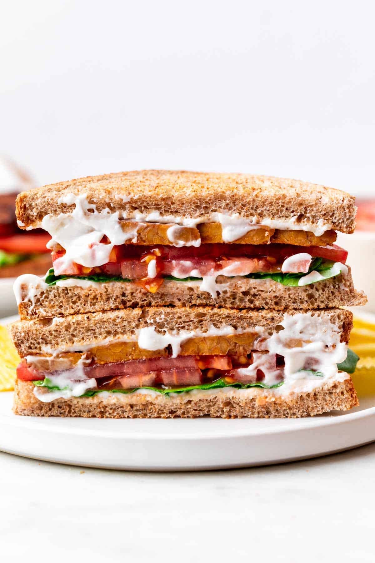 Vegan BLT sandwich cut in half and served with potato chips on a white plate