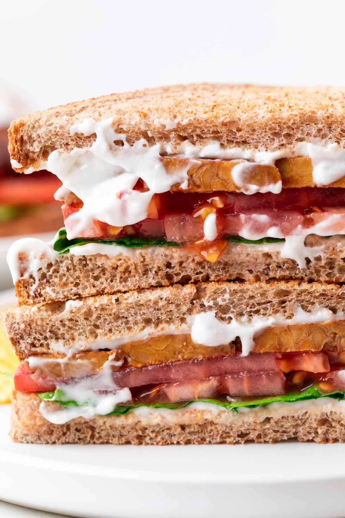 White plate with a Vegan BLT sandwich sliced in half and a side of potato chips
