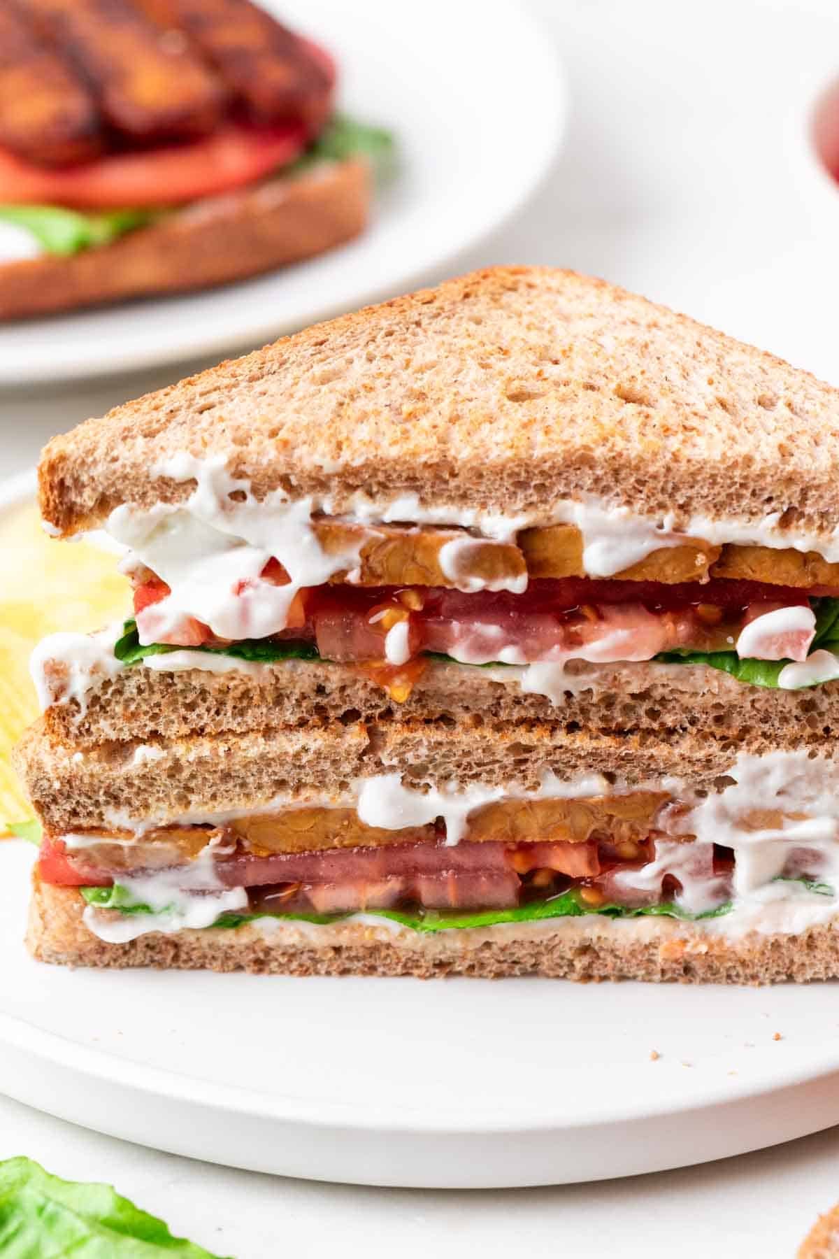 Halved Vegan BLT sandwich with vegan bacon, lettuce, and tomato served with potato chips