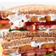 Vegan BLT sandwich cut in half on a white plate with crispy potato chips