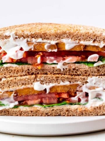 Vegan BLT sandwich halves stacked on a white plate with potato chips on the side
