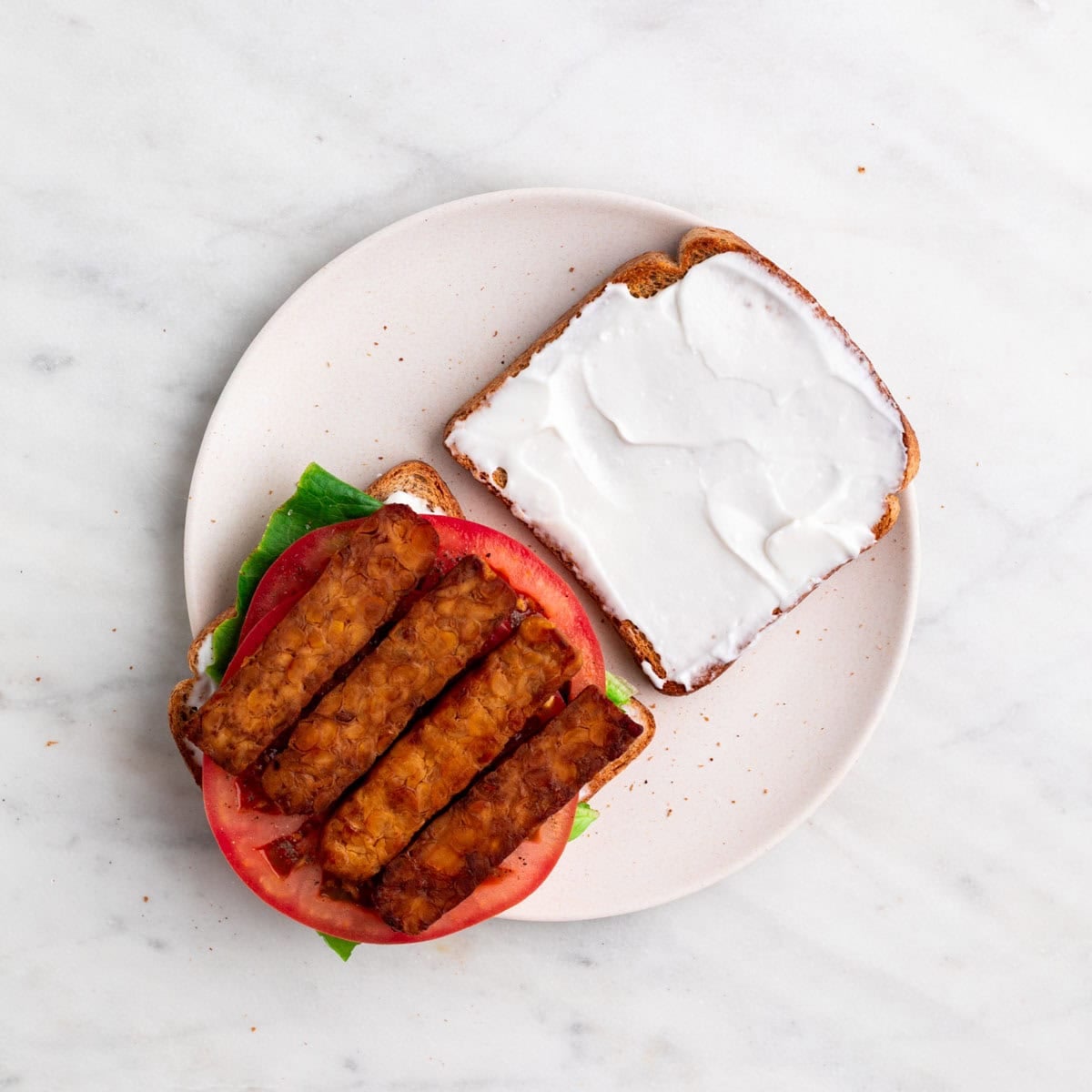 Cooked vegan bacon arranged over the lettuce and tomato