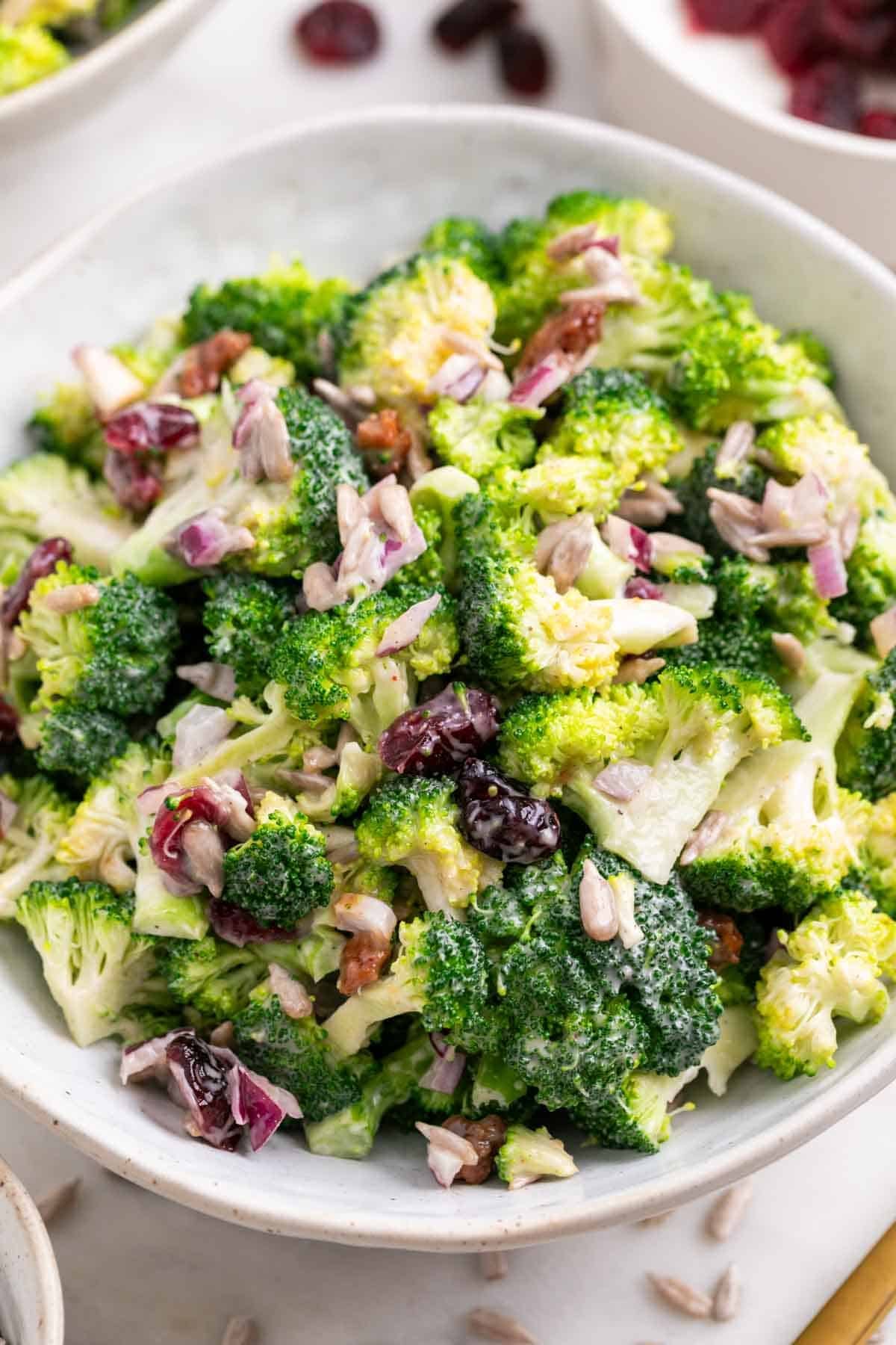 Two bowls of creamy vegan broccoli salad on a white surface