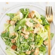 Vegan Caesar salad served on a plate with a fork and extra cheese on marble