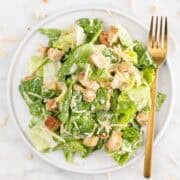 Vegan Caesar salad on a plate with a fork and scattered vegan Parmesan on marble