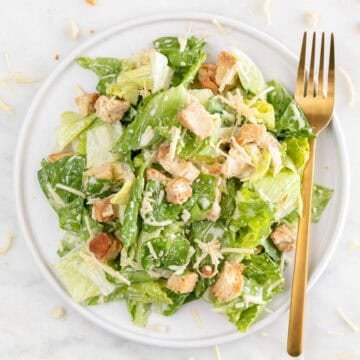Vegan Caesar salad on a plate with a fork and scattered vegan Parmesan on marble