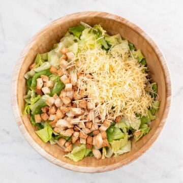 Romaine lettuce, vegan croutons, and shredded vegan cheese in a large bowl