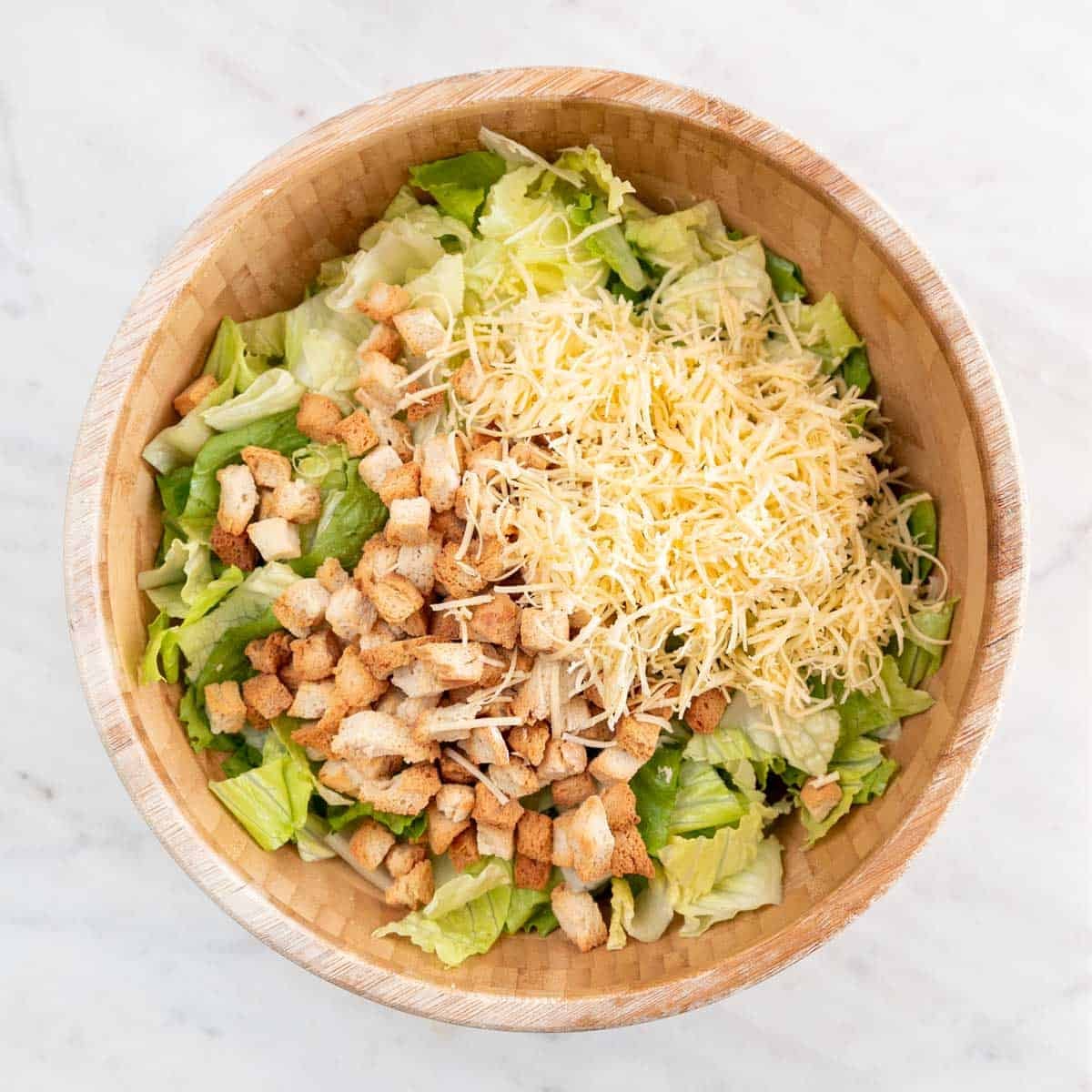 Romaine lettuce, vegan croutons, and shredded vegan cheese in a large bowl
