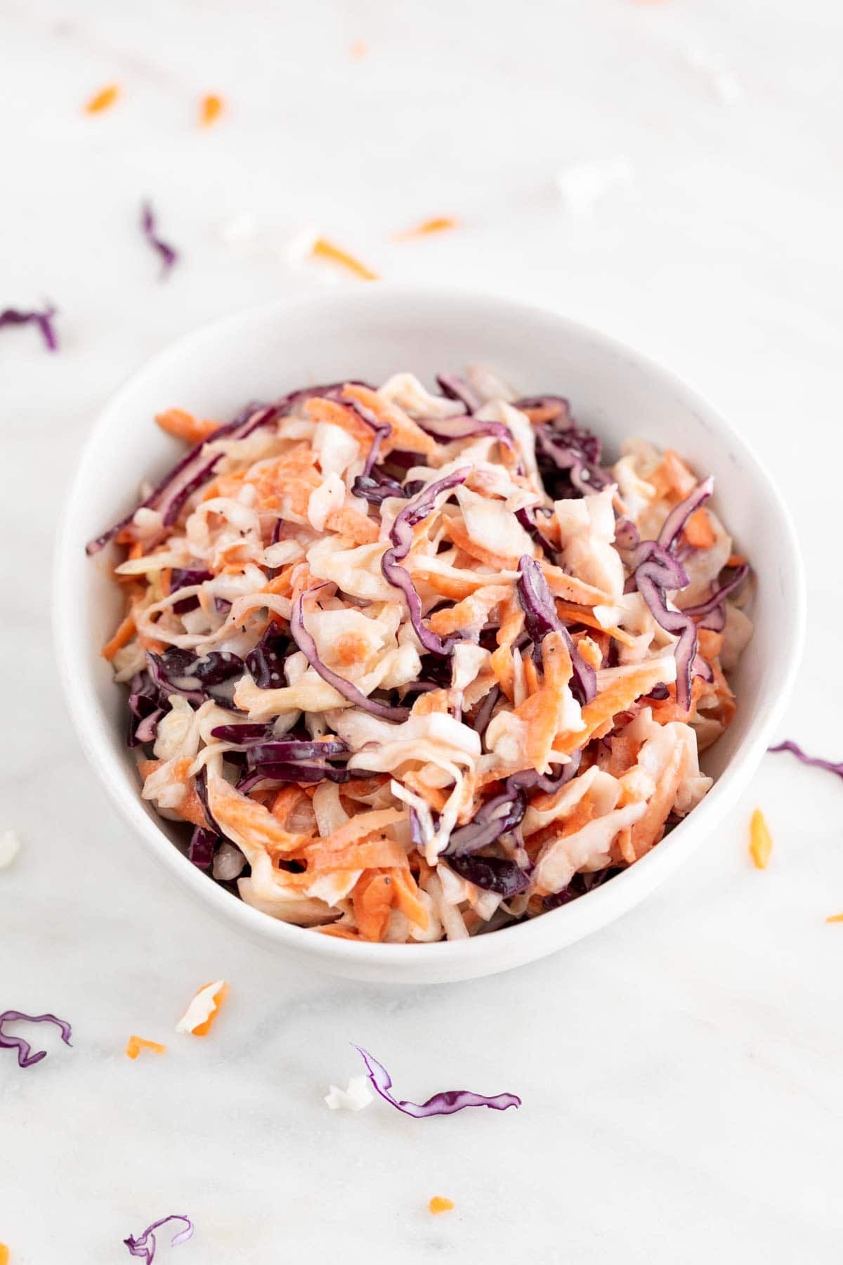 Creamy vegan coleslaw in a white bowl on marble