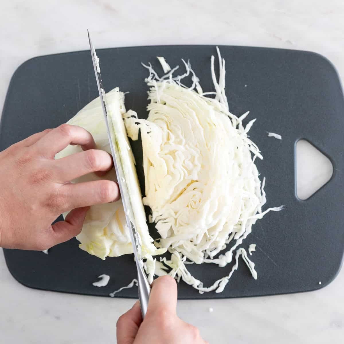 Thinly slicing cabbage with a knife on a cutting board