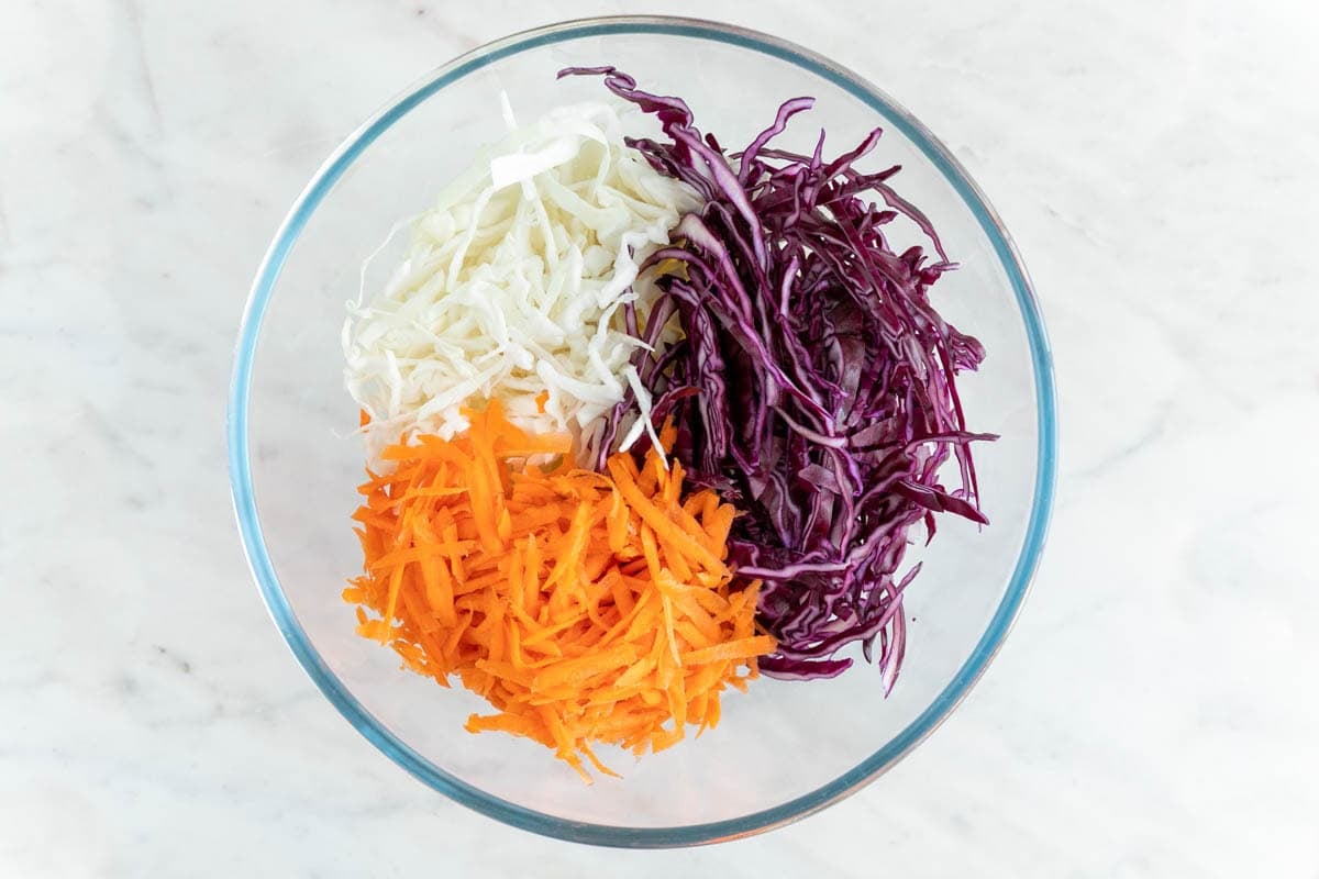 Shredded green cabbage, red cabbage, and carrot in a large bowl
