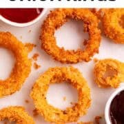 Crispy onion rings arranged beside ketchup and barbecue sauce on a white surface