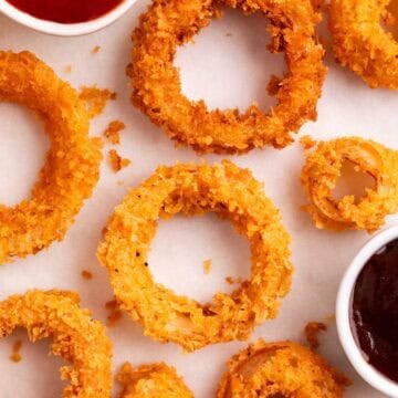 Crunchy onion rings with barbecue sauce and ketchup in small dipping bowls on a white background