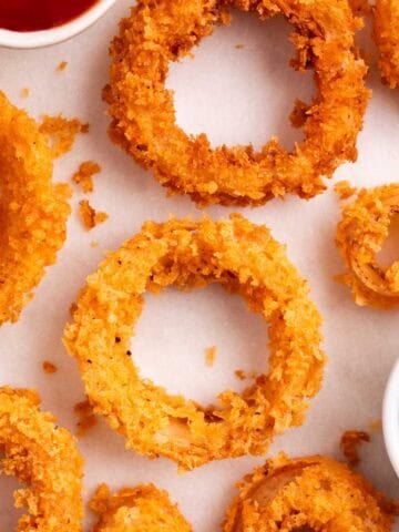 Crunchy onion rings with barbecue sauce and ketchup in small dipping bowls on a white background