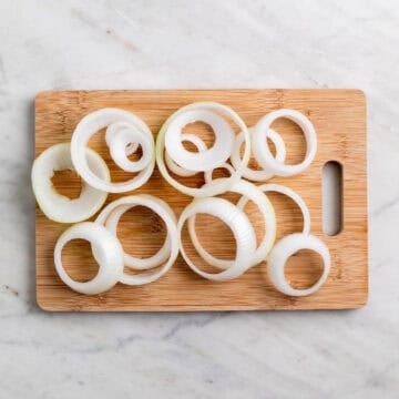 Onion rings sliced from a large yellow onion on a wooden cutting board