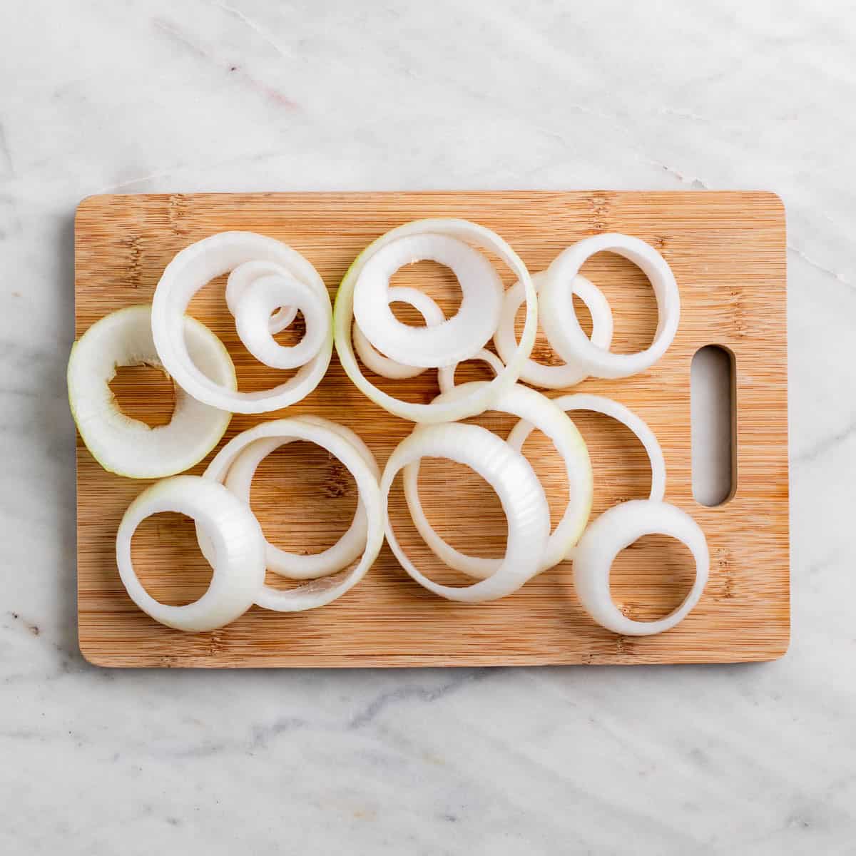 Onion rings sliced from a large yellow onion on a wooden cutting board