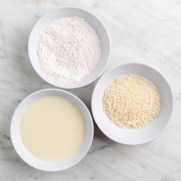 Three shallow bowls with flour and spices, soy milk and cornstarch, and breadcrumbs