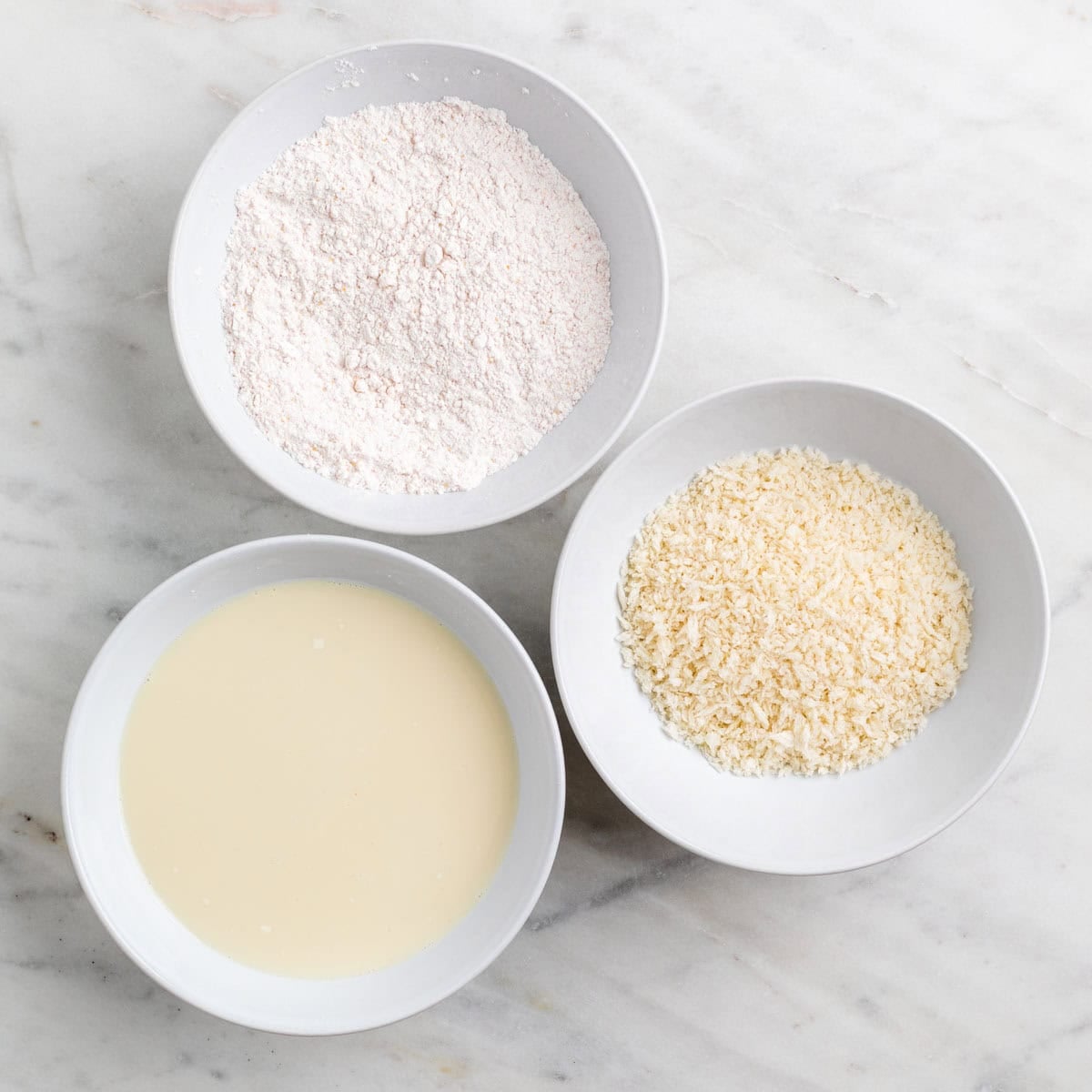 Three shallow bowls with flour and spices, soy milk and cornstarch, and breadcrumbs