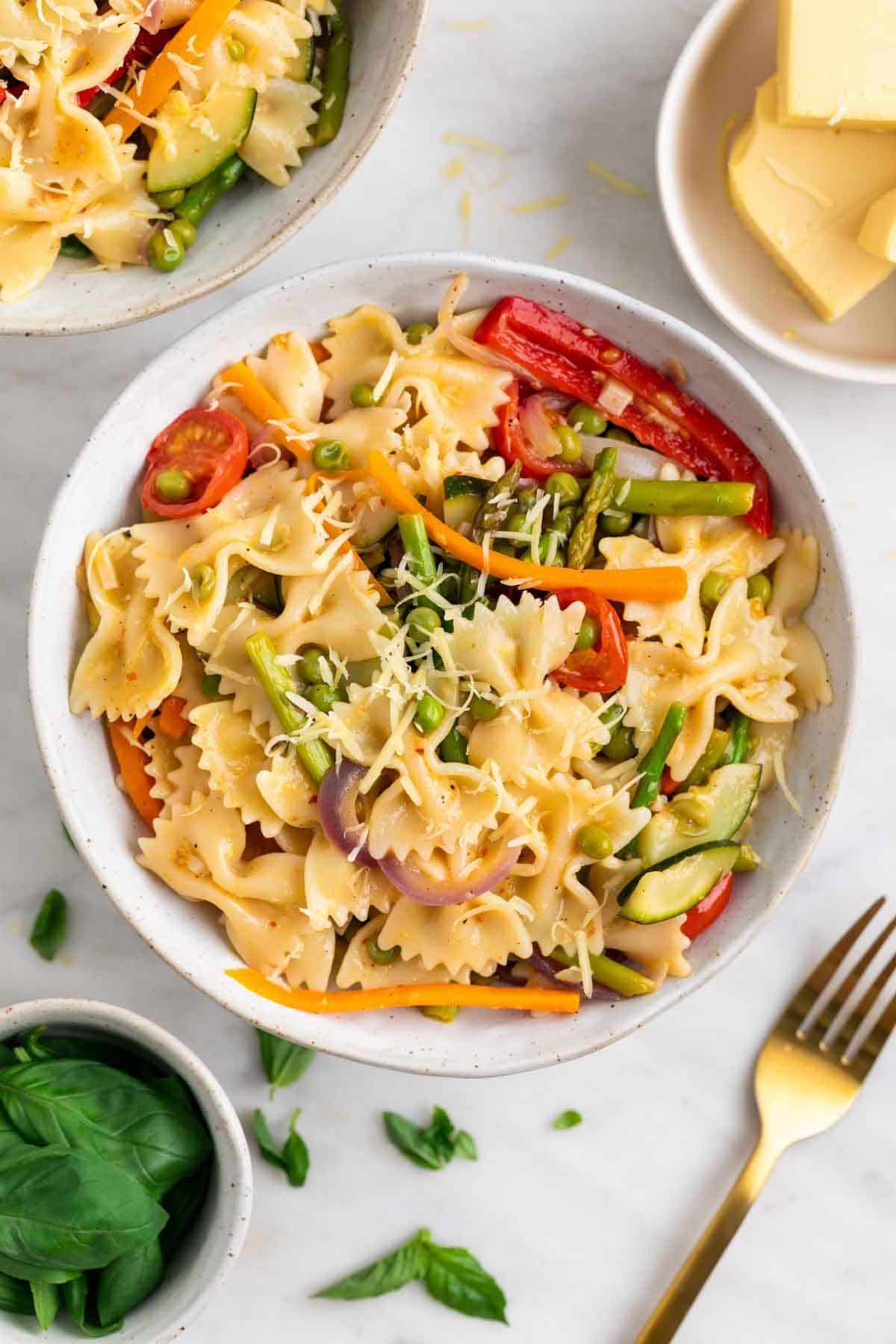 Two plates of vegan pasta primavera topped with vegan cheese and fresh basil
