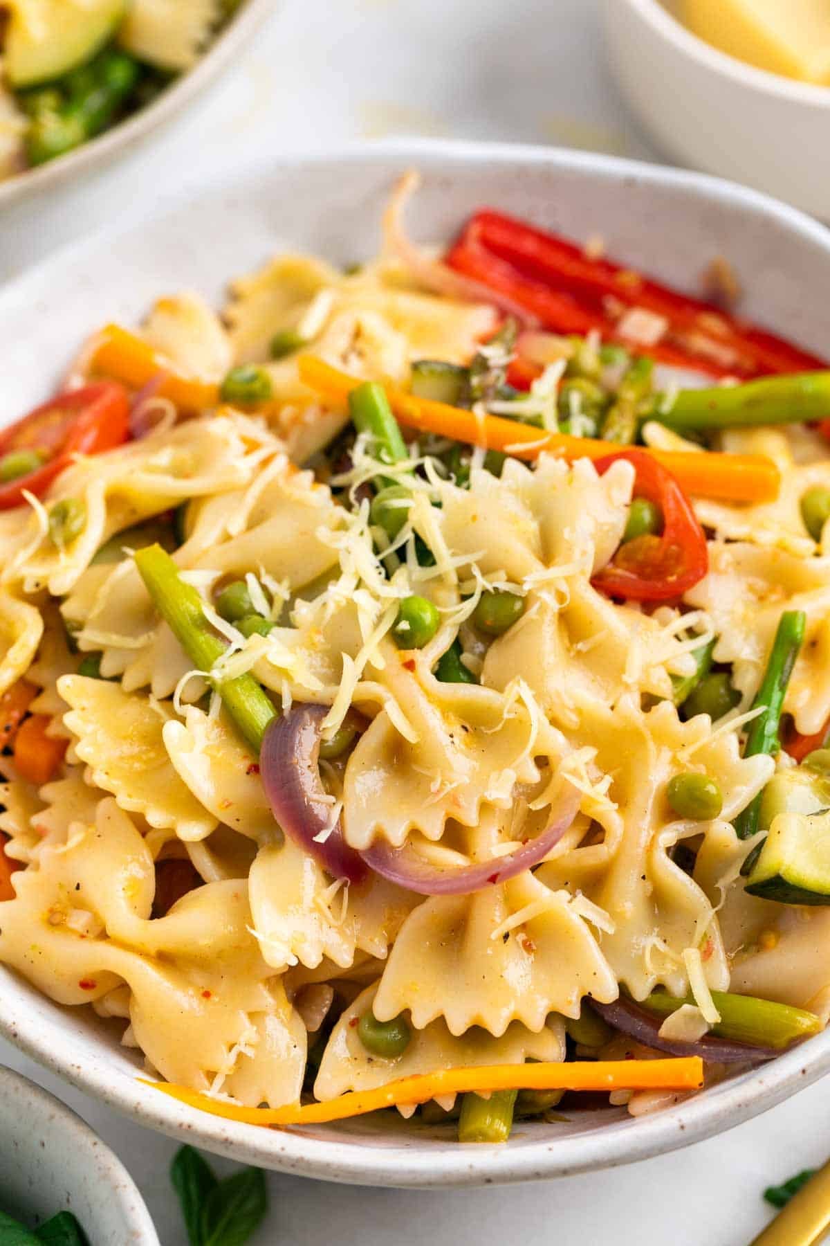 Vegan pasta primavera served in two bowls with extra vegan cheese and basil