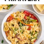 Two bowls of vegan pasta primavera garnished with fresh basil and vegan cheese