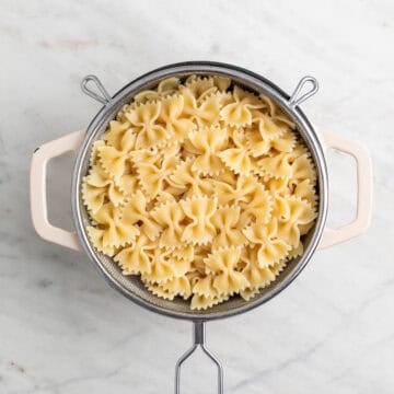 Cooked farfalle draining in a colander over a pot