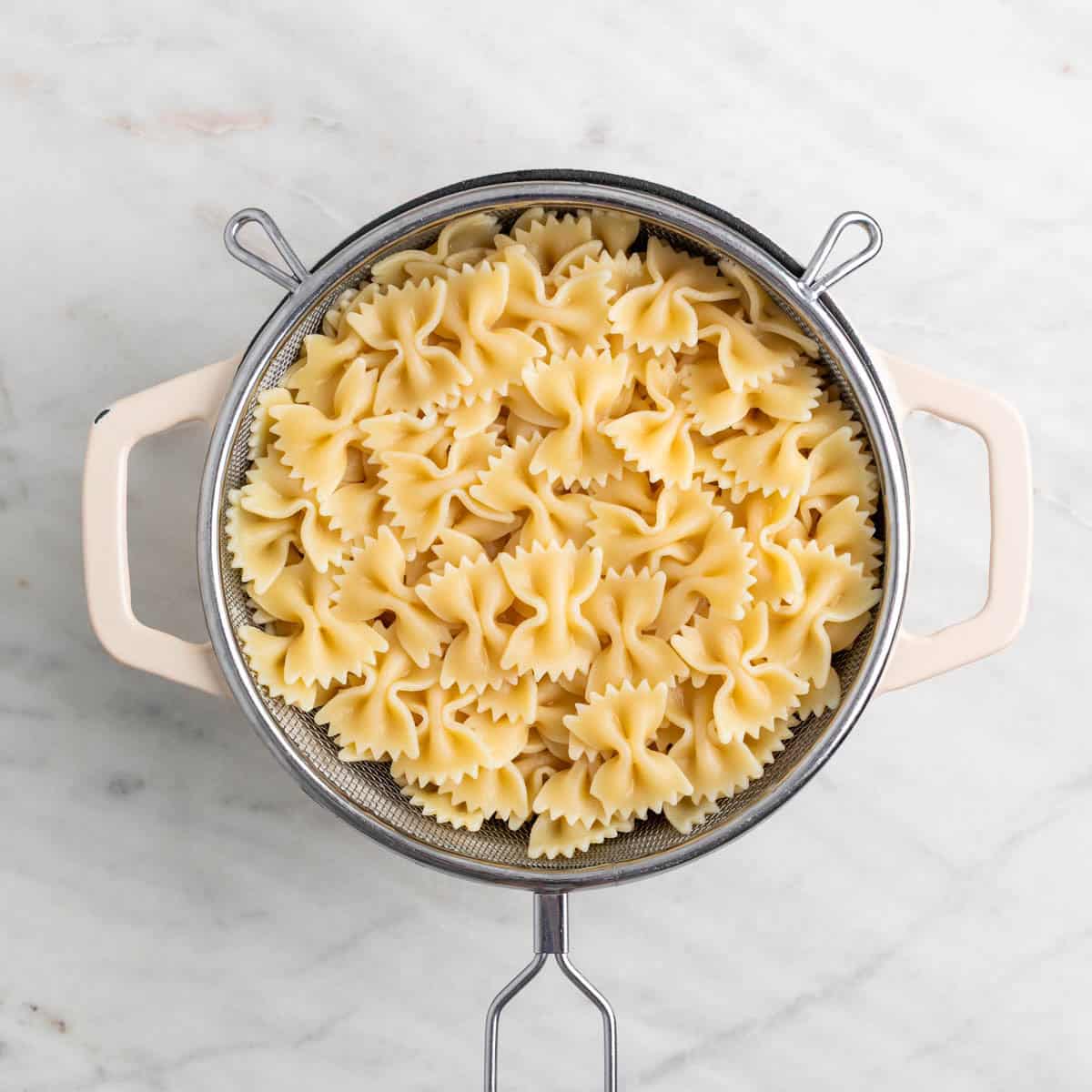 Cooked farfalle draining in a colander over a pot