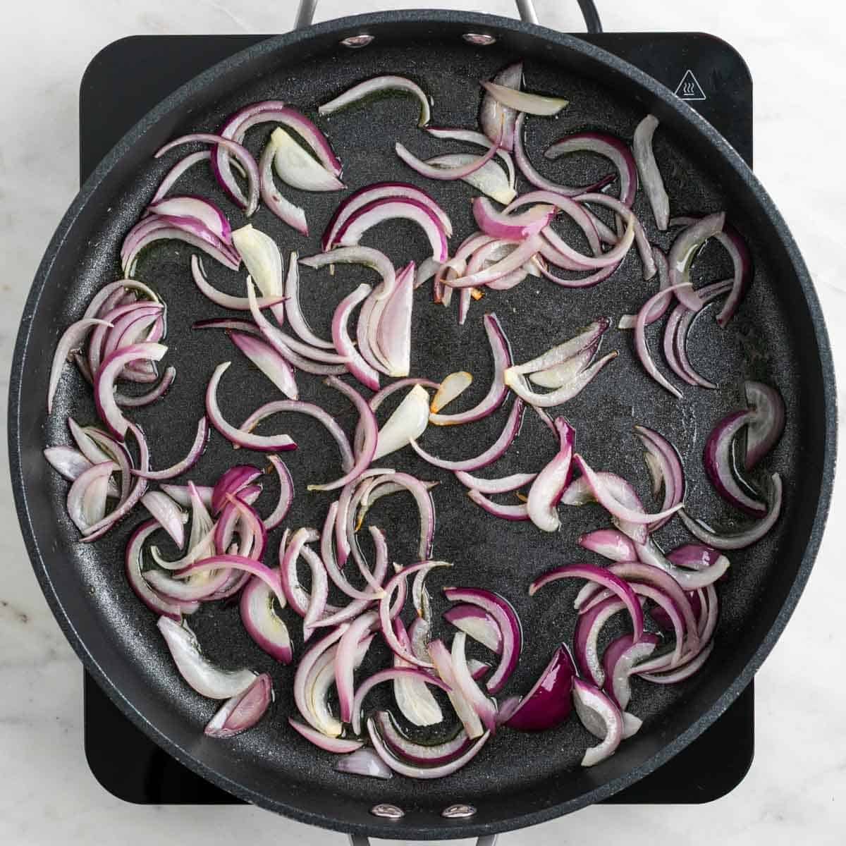 Sliced red onion cooking in olive oil in a large skillet