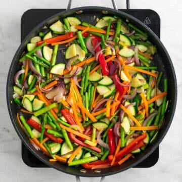 Asparagus, carrot, zucchini, and red bell pepper cooking in a skillet